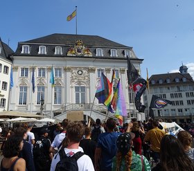 Der Demozug ist auf dem Marktplatz angekommen; im Hintergrnd das alte Rathaus.  Rechts ist ein Banner mit der Aufschrift "Bonn bleibt bunt" zu sehen.